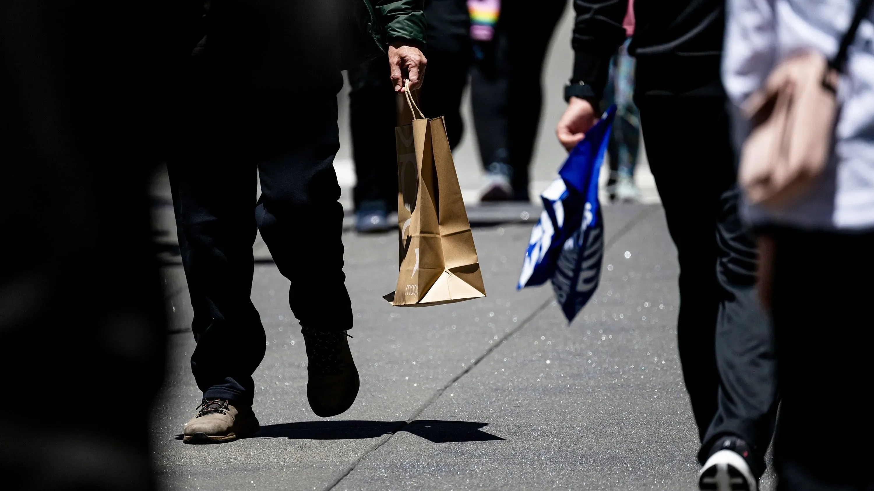 مشاة يحملون أكياس تسوق في منطقة حضرية، مما يعكس تراجع ثقة المستهلكين وتأثير التعريفات الجمركية على الإنفاق.