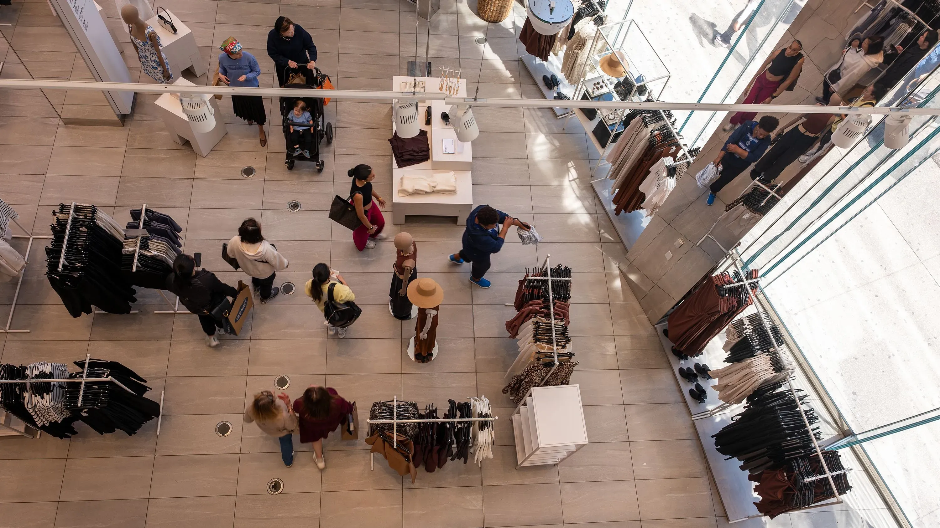 متسوقون يتجولون في متجر ملابس عصري، معروضات متنوعة من الملابس، مما يعكس تراجع إنفاق المستهلكين في أبريل.