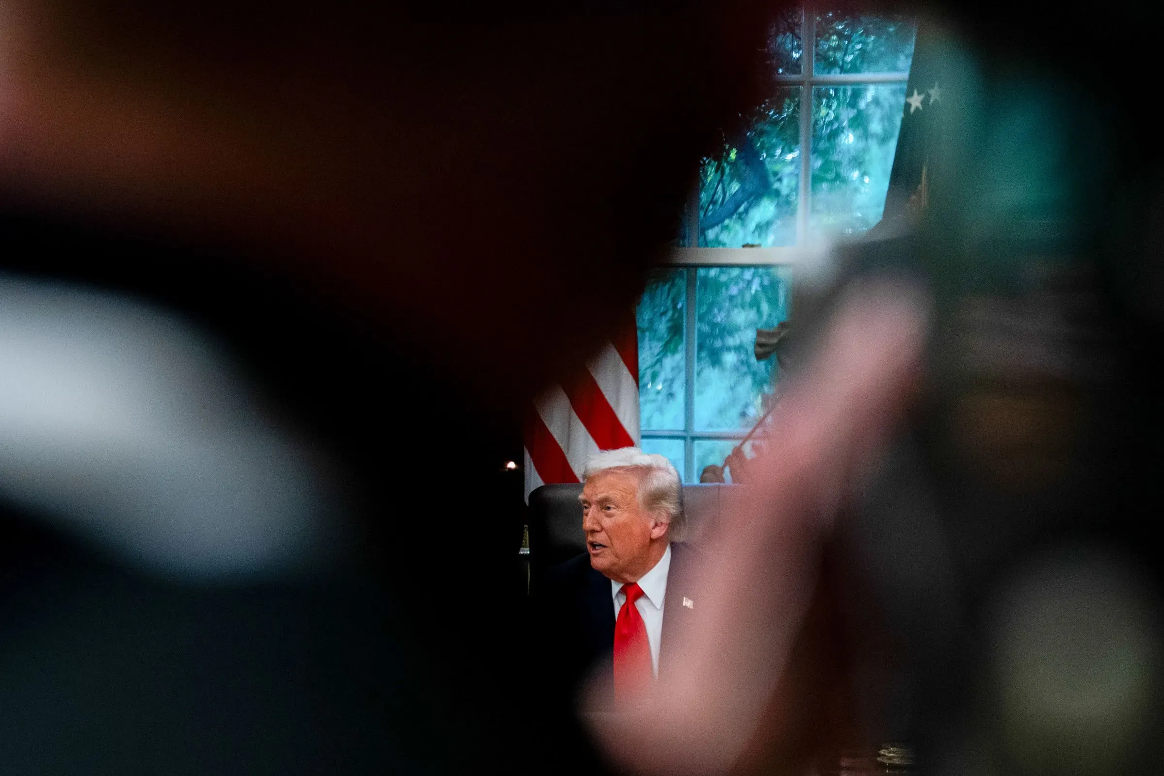 صورة تظهر الرئيس ترامب في المكتب البيضاوي، محاطًا بأضواء الكاميرات، مما يعكس أجواء التوتر السياسي حول التحقيقات القانونية.