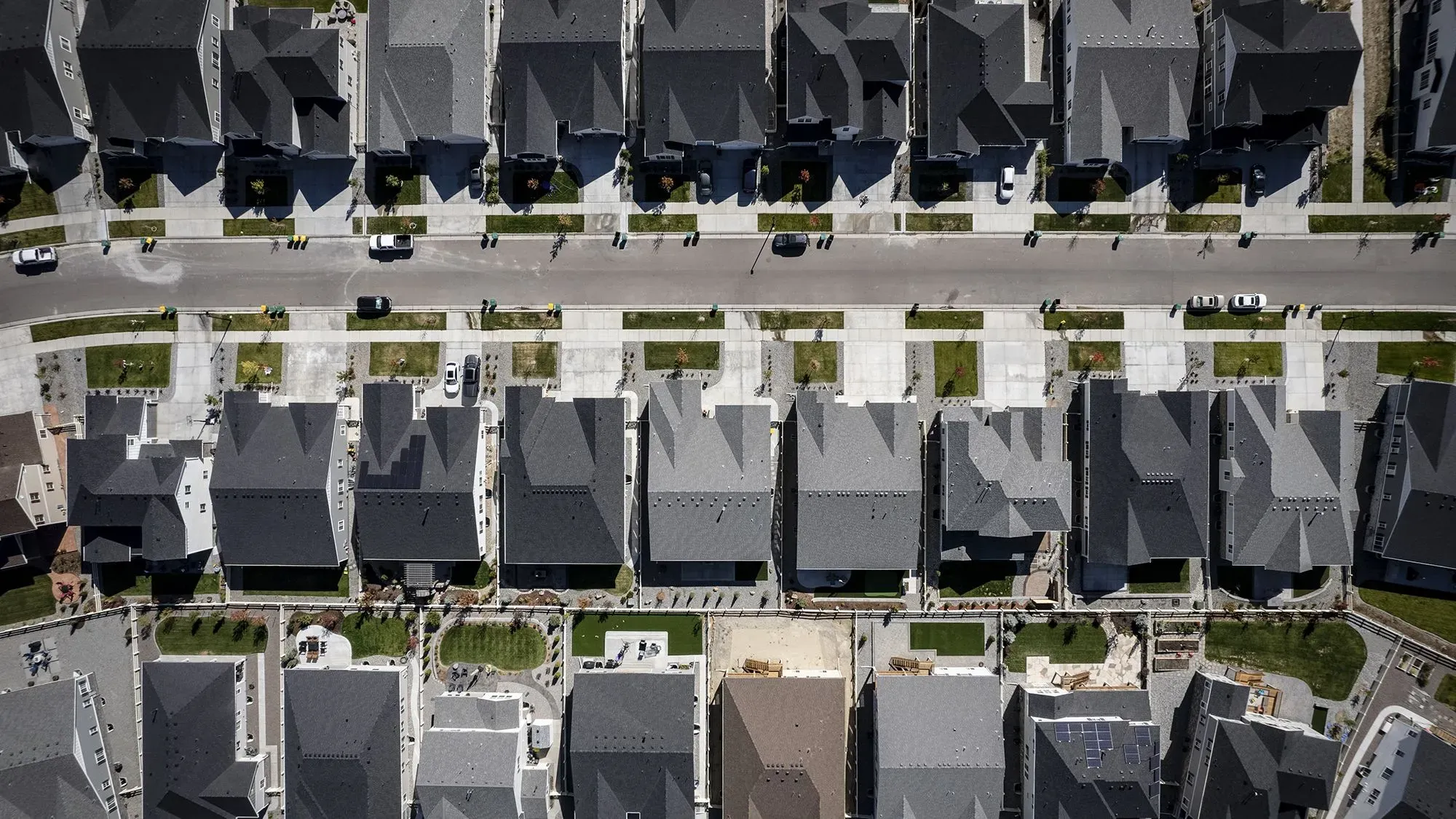 مشهد جوي لحي سكني في الولايات المتحدة يظهر صفوف من المنازل ذات الأسطح الداكنة، مع وجود سيارات في الشوارع والأرصفة.