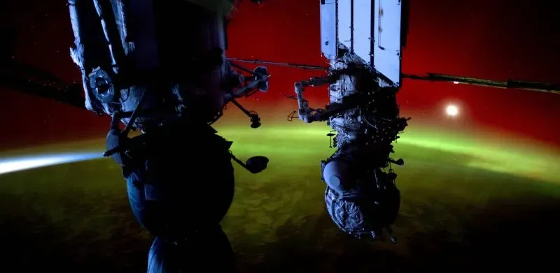 صورة مذهلة تُظهر محطة الفضاء الدولية مع شروق الشمس خلفها، بينما تُضيء الأضواء الشمالية السماء بلون أخضر زاهي.