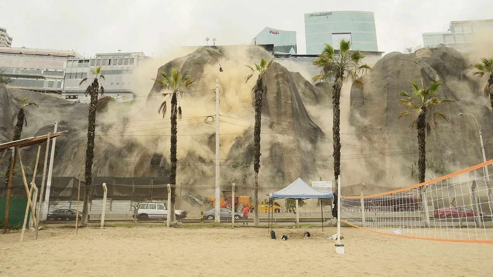 تساقط الحجارة من جرف صخري في ليما بعد زلزال، مع ظهور رمال وغبار، وأشجار نخيل ومرافق رياضية في المشهد.