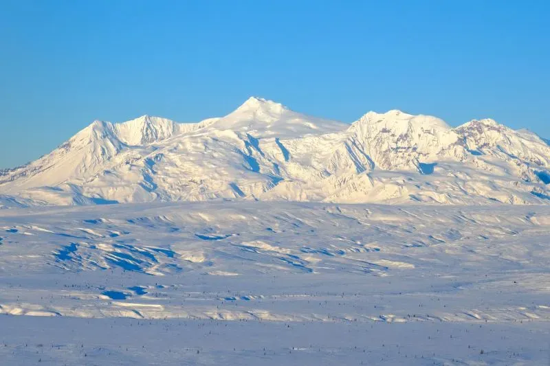 بركان جبل سبير في ألاسكا، مغطى بالثلوج تحت سماء زرقاء، يظهر علامات نشاط زلزالي قد تشير إلى احتمال ثورانه قريبًا.