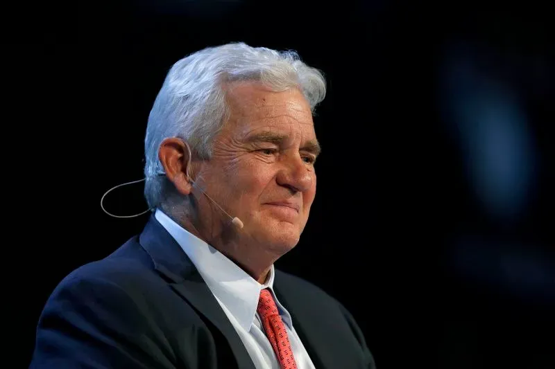 صورة لرجل مسن ذو شعر أبيض، مبتسم، يرتدي بدلة رسمية، يتحدث في مؤتمر. تعكس تعابيره الثقة والقيادة في سياق قضية قانونية معقدة.