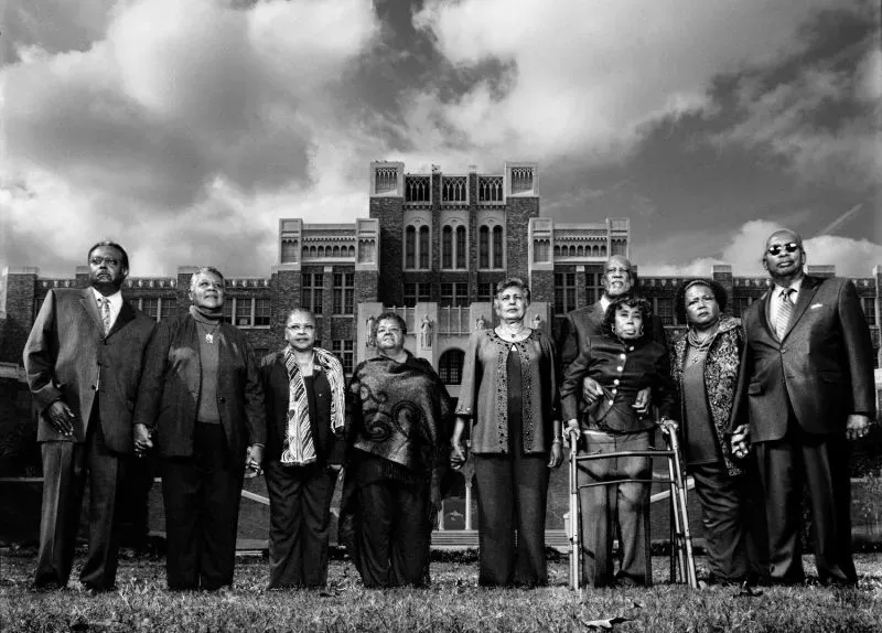 مجموعة من الأشخاص البالغين يقفون معًا أمام مبنى تاريخي، يعبرون عن التضامن في مواجهة التحديات القانونية والسياسية.