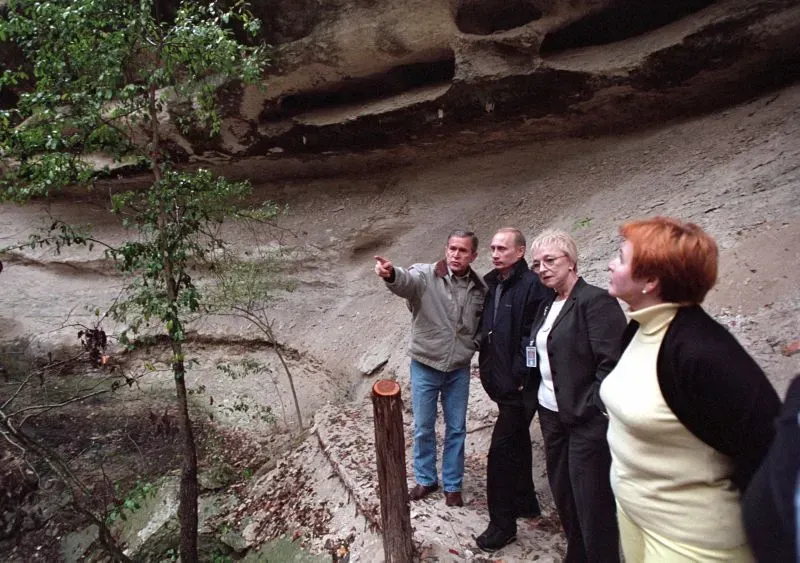 زيارة غير رسمية بين جورج بوش وفيدير بوتين، حيث يتحدثان معًا في موقع طبيعي، مع وجود موظفين آخرين في الخلفية.