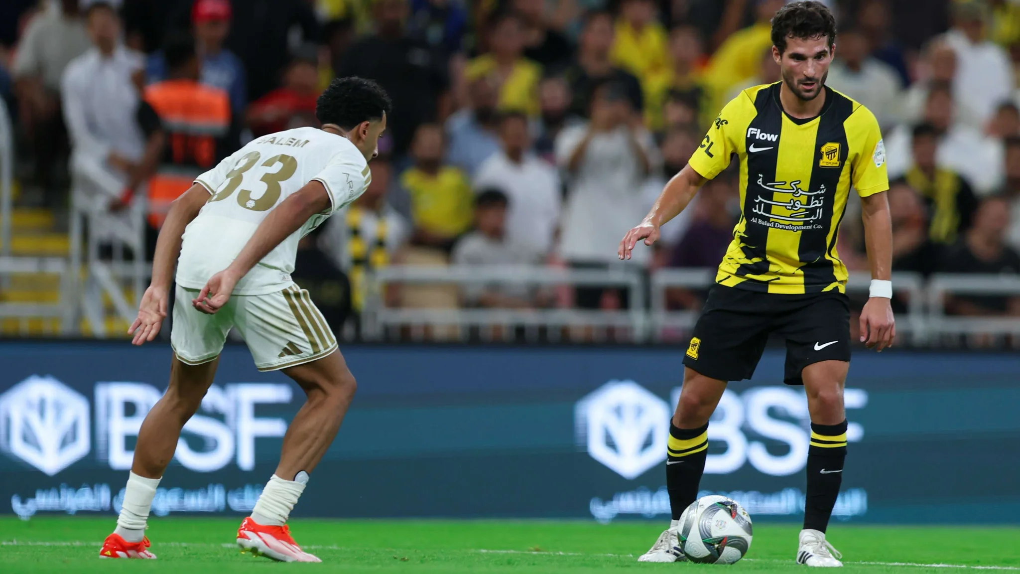لاعب من الاتحاد بالزي الأصفر والأسود يسيطر على الكرة أمام لاعب النصر الأبيض خلال كلاسيكو سعودي يشهد ضغطاً تكتيكياً عالي المستوى.