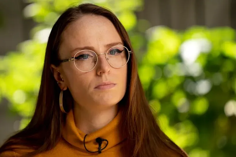 آنا ليس، إحدى المساعدات السابقات، تظهر في مقابلة مع خلفية خضراء، تعبر عن تجاربها مع سوء السلوك في مكتب الحاكم السابق.