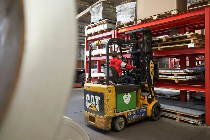 عامل يستخدم رافعة شوكية لنقل قطع غيار السيارات في مستودع، مما يعكس تأثير الرسوم الجمركية الجديدة على الصناعة.