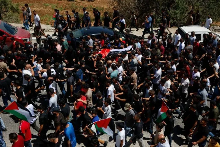 تجمع حشود من الفلسطينيين في مسيرة احتجاجية في الضفة الغربية، حاملين الأعلام الفلسطينية، تنديدًا بمقتل خميس عياد.