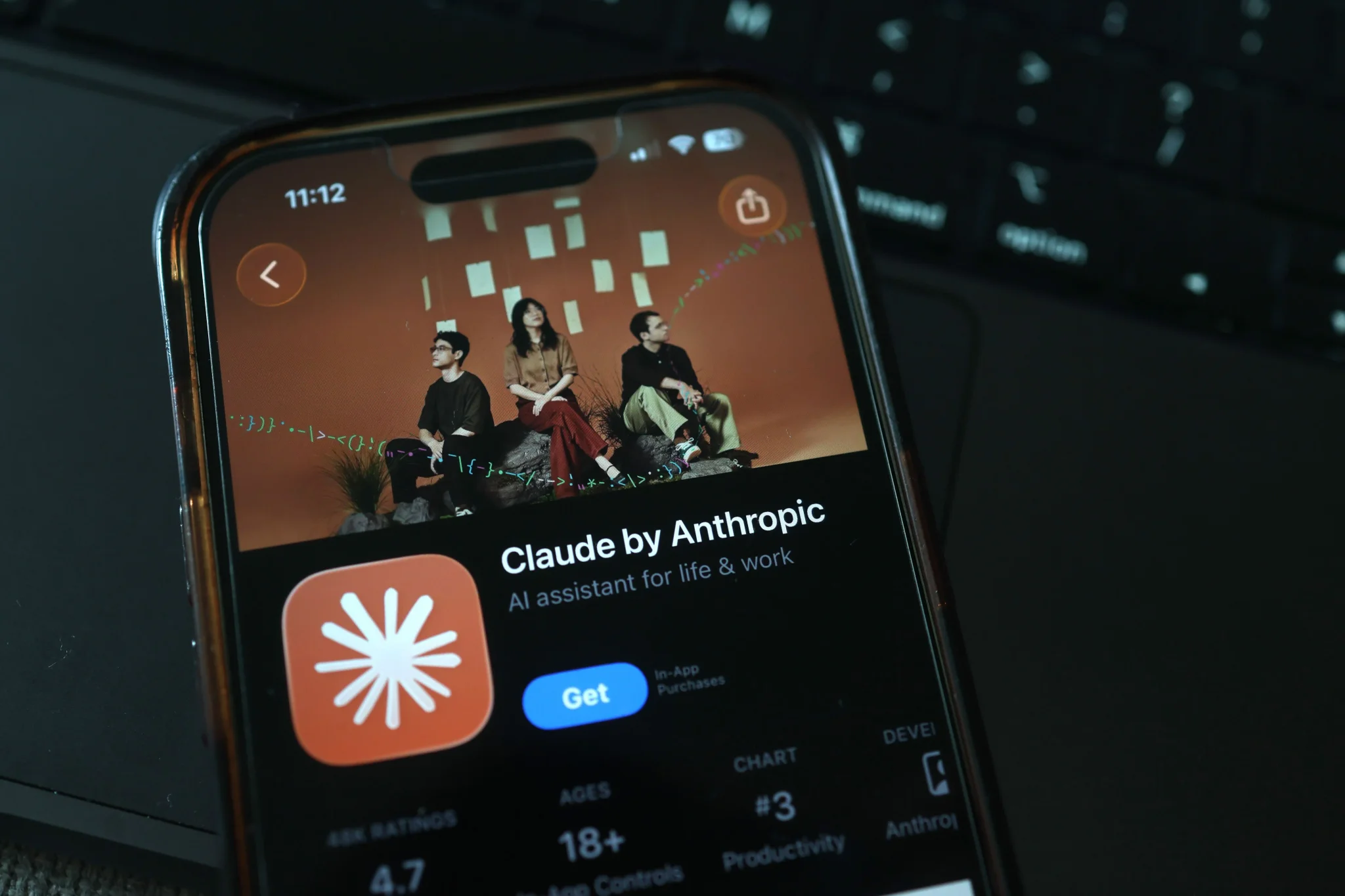 تطبيق Claude من شركة Anthropic يظهر على شاشة هاتف ذكي، مع خلفية ملونة وأشخاص يجلسون معًا، مما يعكس تأثير الذكاء الاصطناعي في الحياة اليومية.