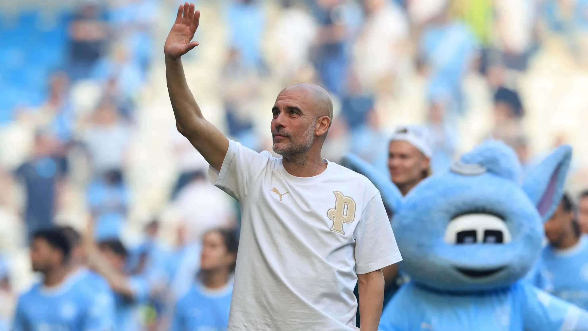 المدرب بيب غوارديولا يلوح بيده وسط جمهور ملعب كرة قدم، في سياق بحث الاتحاد الإيطالي عن مدرب جديد للمنتخب.