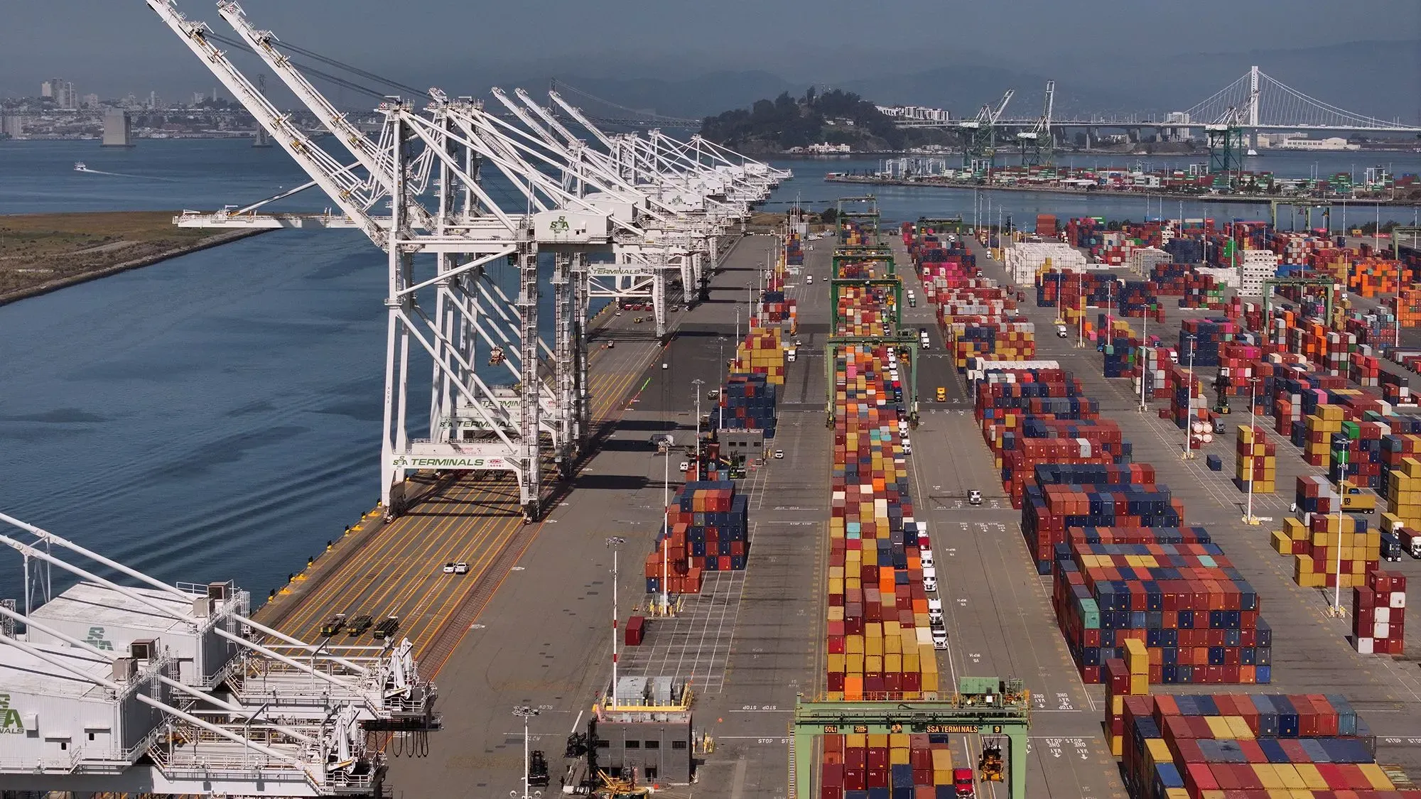 صورة لميناء مزدحم بالحاويات الملونة، مع رافعات تحميل ضخمة على الأرصفة، تعكس تأثير التعريفات الجمركية على التجارة.