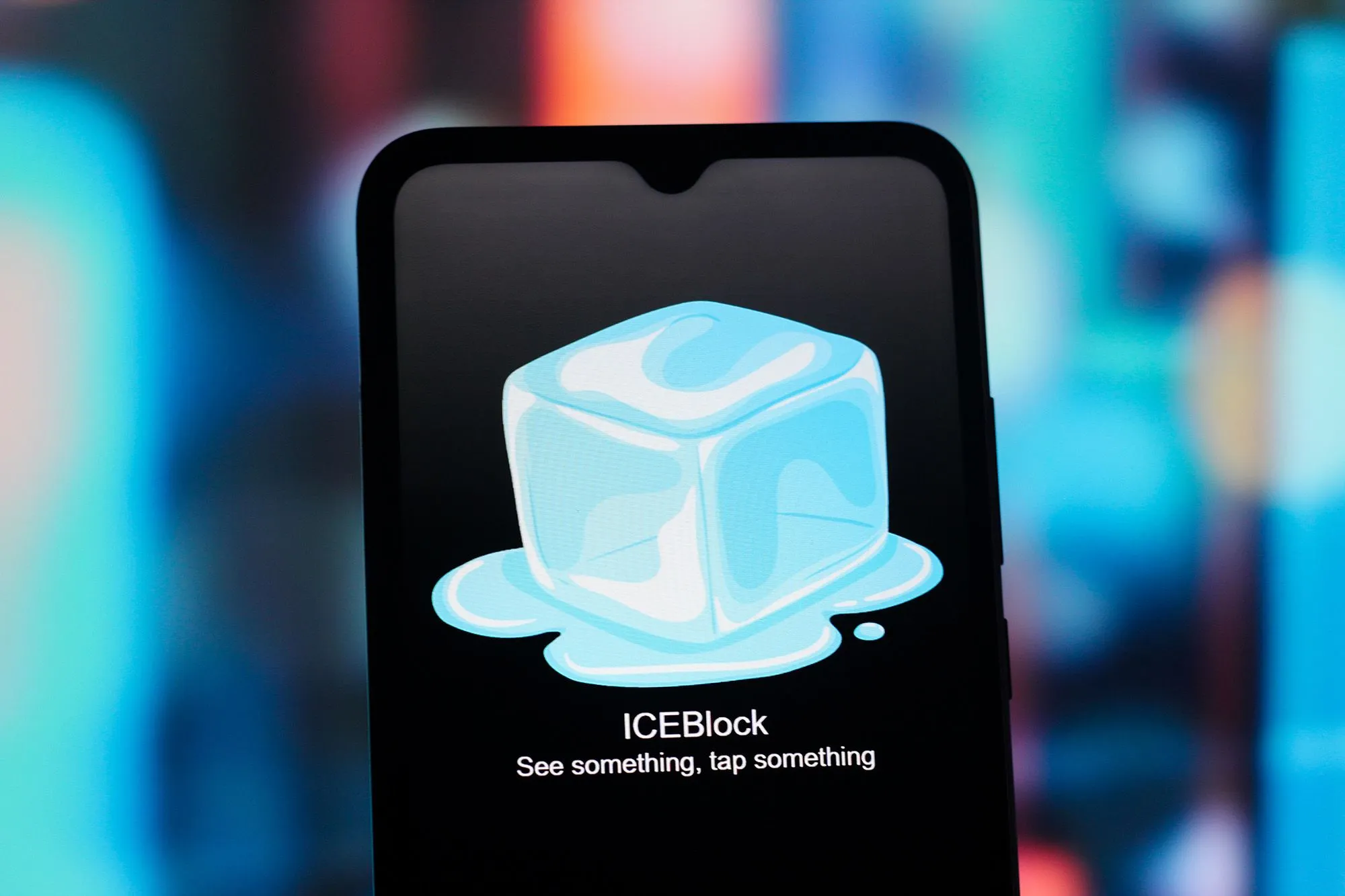 شعار تطبيق ICEBlock على شاشة هاتف ذكي، يظهر مكعب ثلج يذوب مع رسالة تحذيرية لمراقبة مواقع عناصر إنفاذ الهجرة والجمارك الأمريكية.