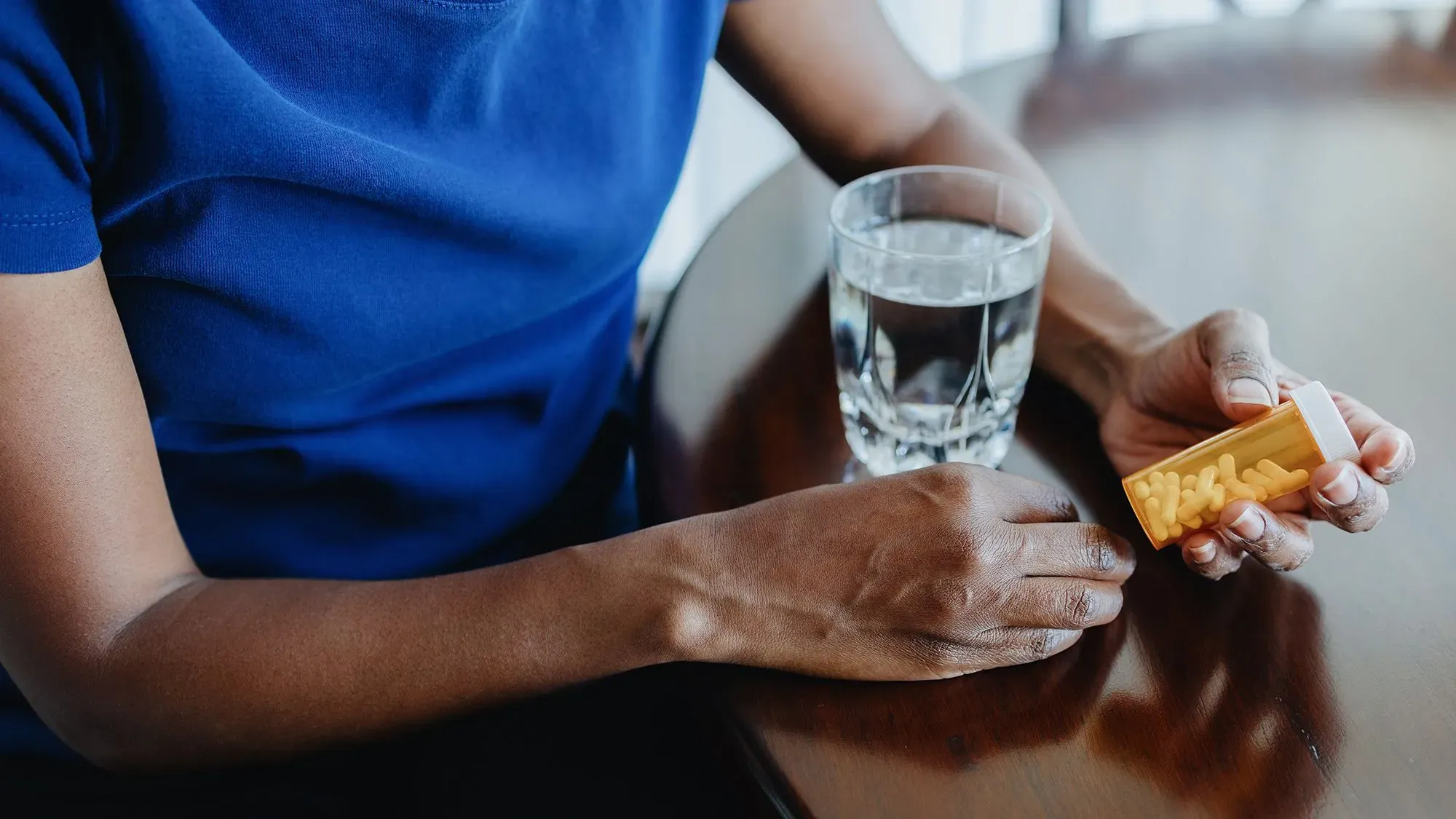 شخص يحمل زجاجة تحتوي على أقراص مضادات الاكتئاب، بجانب كوب من الماء، مما يبرز النقاش حول تأثيرات هذه الأدوية.