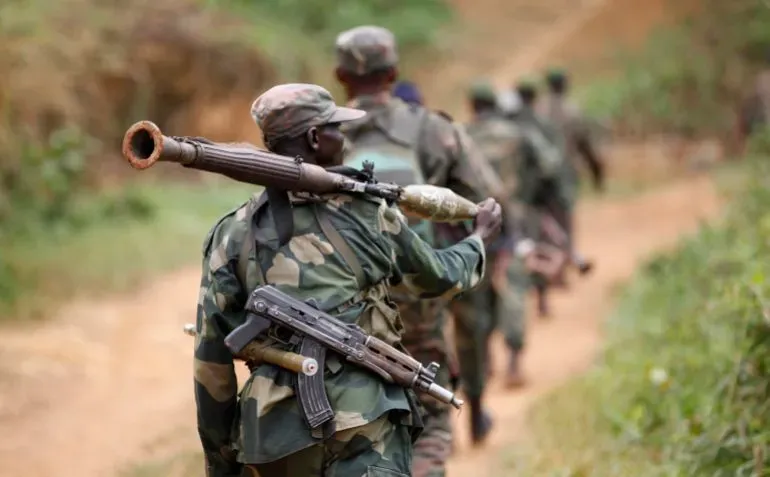 جنود أوغنديون يسيرون في منطقة ريفية، يحمل أحدهم سلاحًا ثقيلًا، مما يعكس التوسع العسكري لأوغندا في شرق جمهورية الكونغو الديمقراطية.