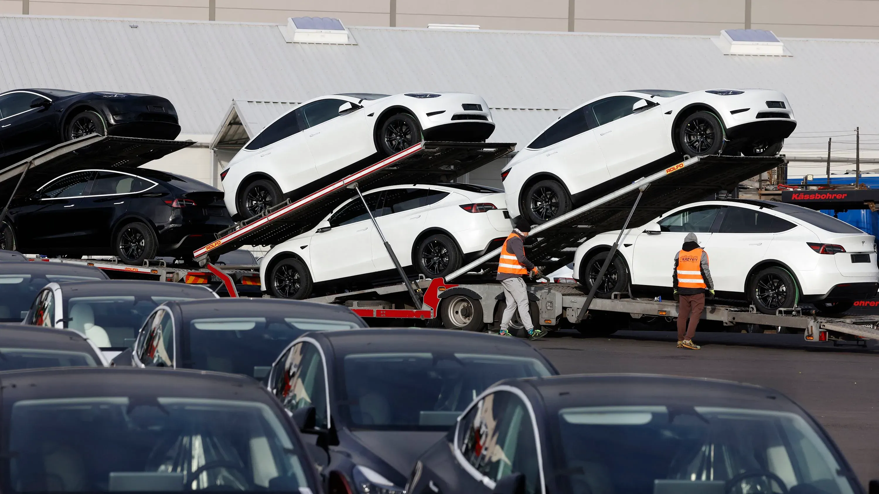 شاحنات تنقل سيارات تسلا الجديدة، مع سيارات بيضاء وسوداء متراكمة، تعكس تراجع مبيعات تسلا وزيادة المنافسة في السوق.