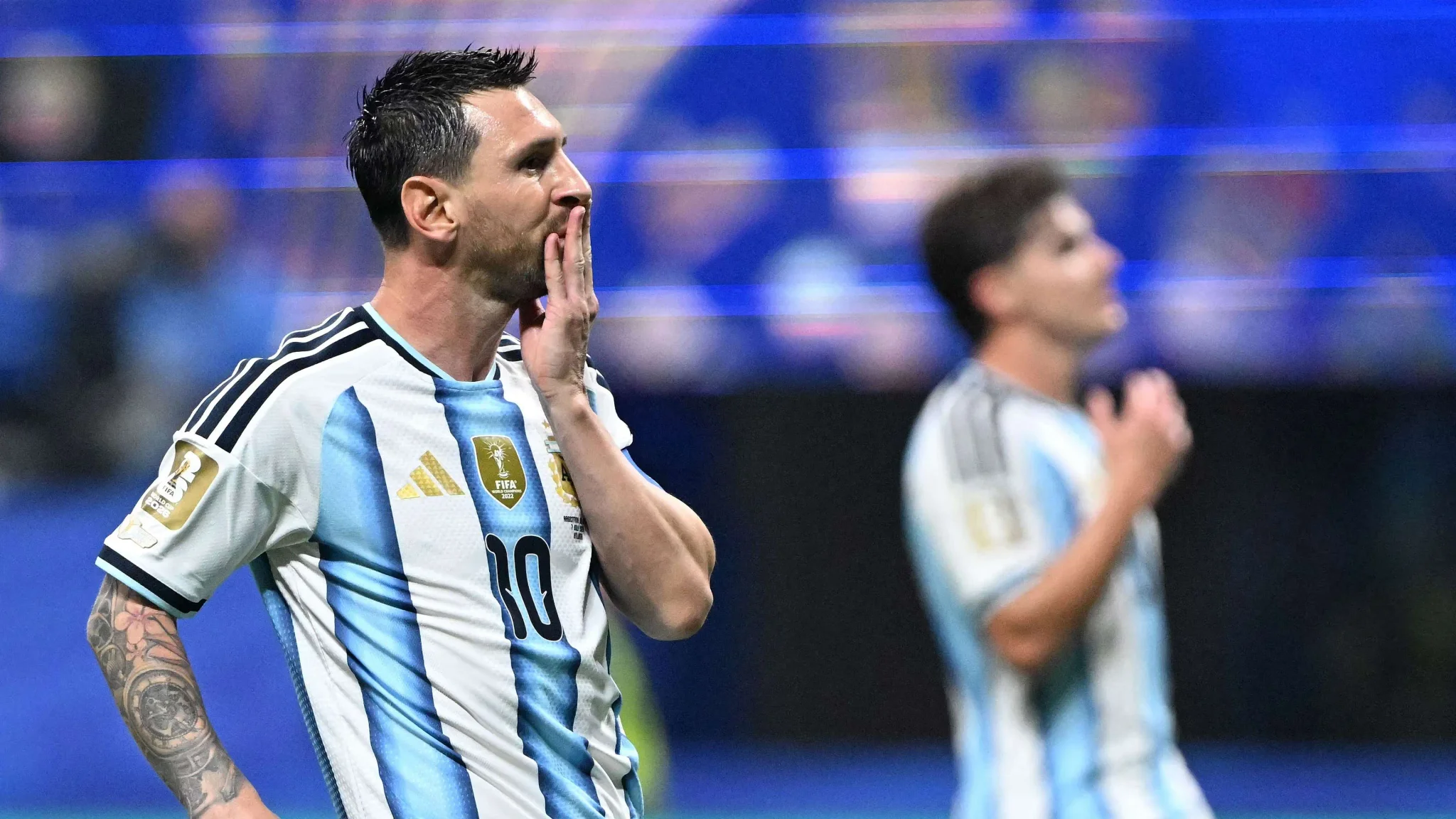 ليونيل ميسي يرتدي قميص الأرجنتين رقم 10 يظهر تعبيراً عاطفياً خلال مباراة كأس العالم، مع خلفية ضبابية للاعب آخر.