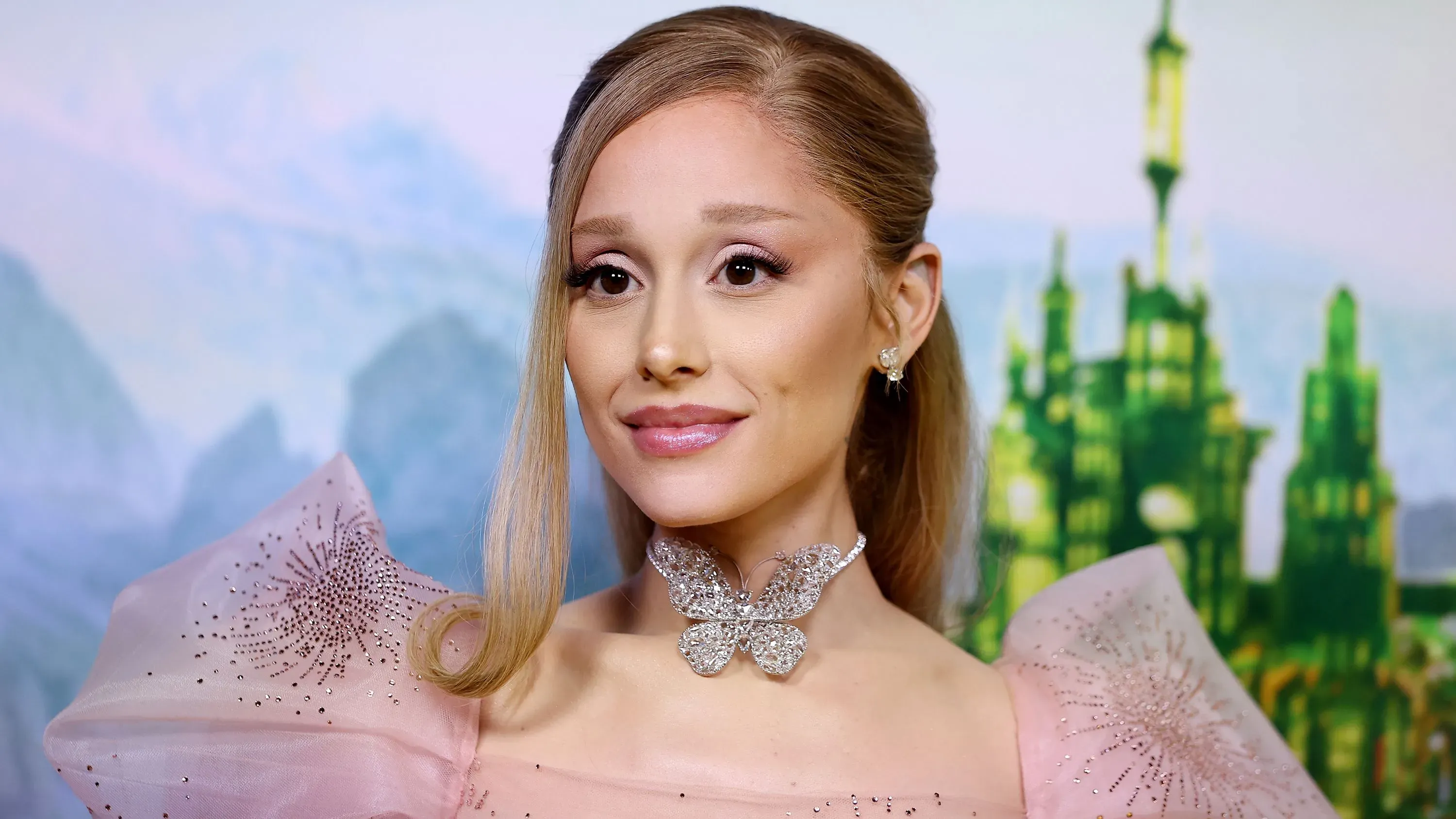 أريانا غراندي مبتسمة أثناء ظهورها في حدث، ترتدي فستانًا أنيقًا مع تفاصيل براقة، تعبيرًا عن فرحها بترشيحها لجائزة الأوسكار.