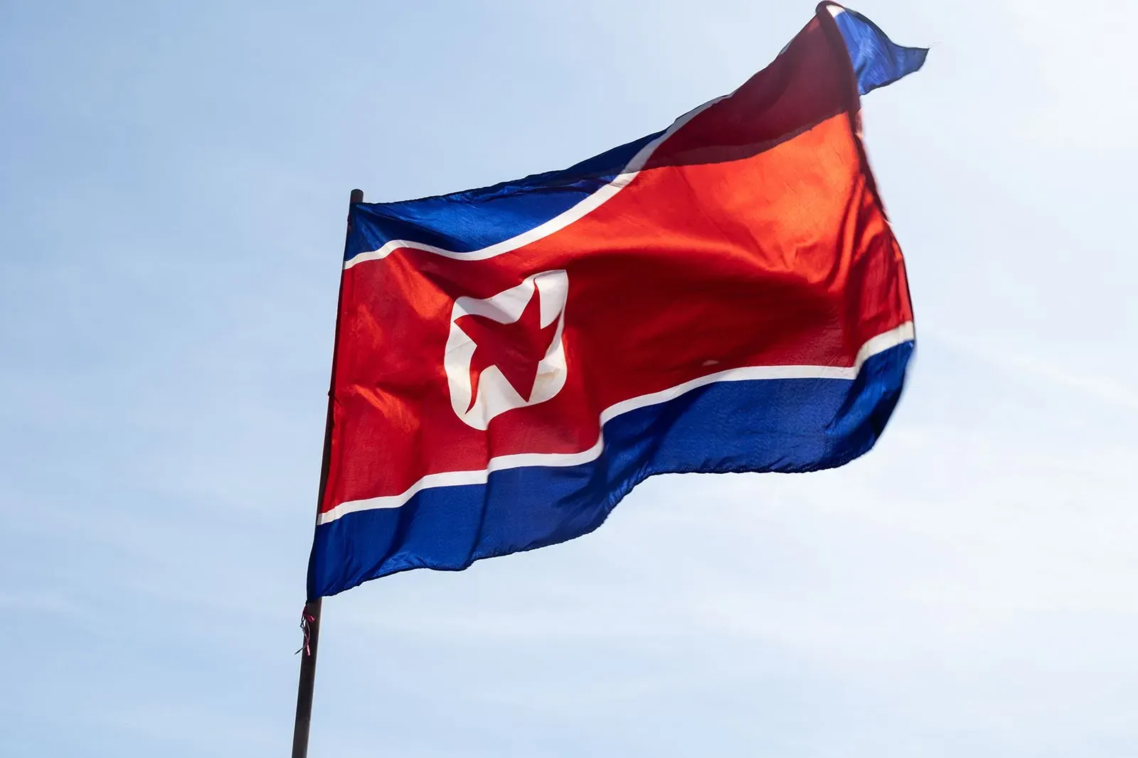 علم كوريا الشمالية يرفرف في السماء، مع ألوانه الزاهية الأحمر والأزرق والأبيض، في سياق حديث عن مخططات احتيال تكنولوجيا المعلومات.