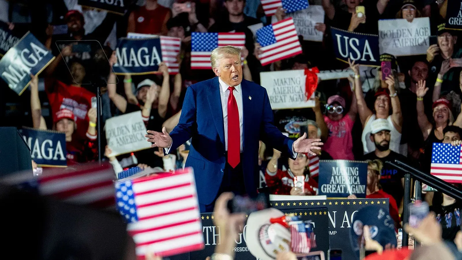 حشود من المؤيدين يحملون لافتات وأعلام أمريكية خلال تجمع لدعم الرئيس ترامب، مع التركيز على تفاعله مع الجمهور.