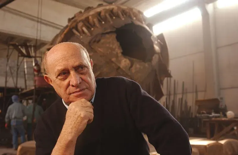 أرنالدو بومودورو، الفنان الإيطالي الشهير، يتأمل أمام إحدى منحوتاته الكروية الضخمة في ورشته، حيث يبرز إبداعه الفني.