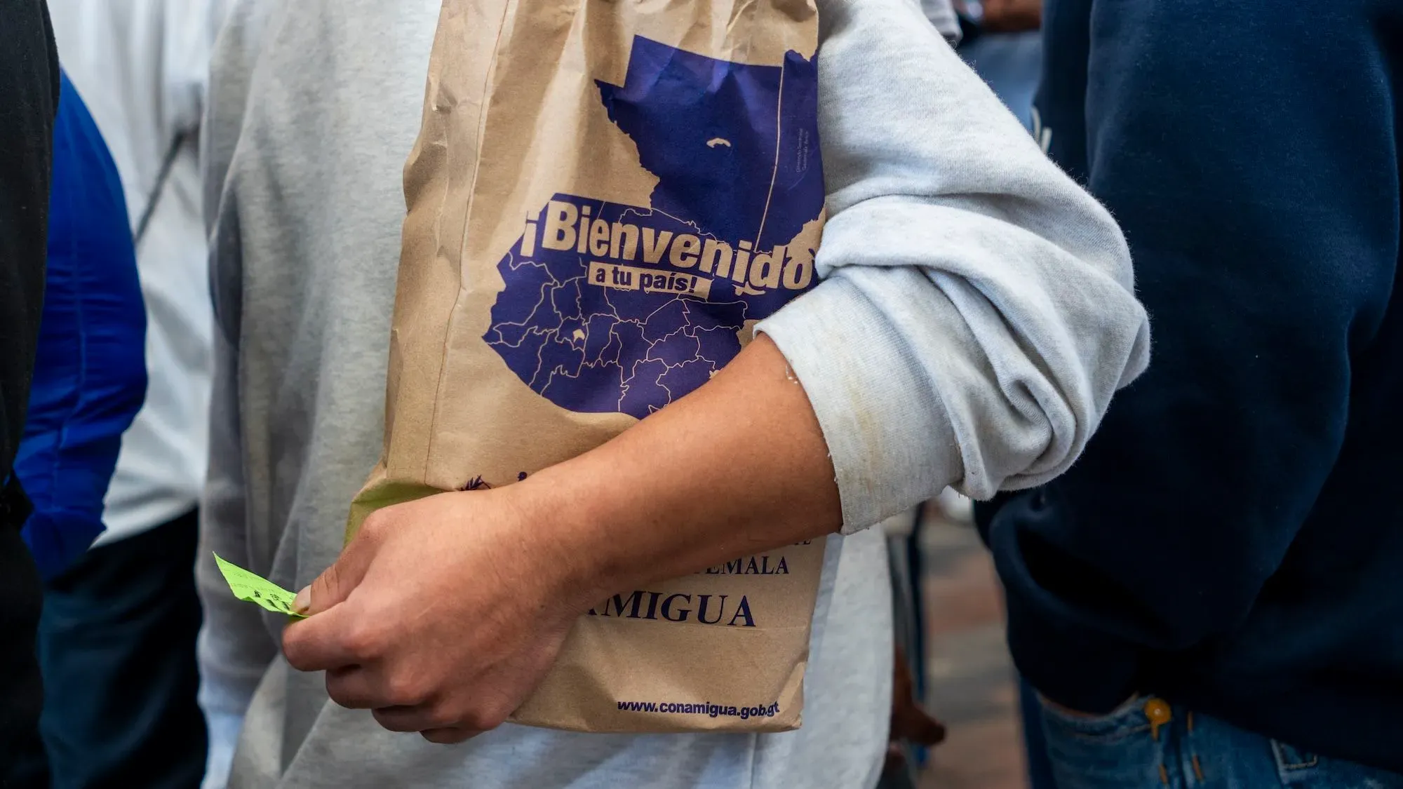 رجل يحمل حقيبة ورقية مكتوب عليها "مرحباً بكم في بلدكم" في مركز استقبال المهاجرين في غواتيمالا بعد رحلة ترحيل.