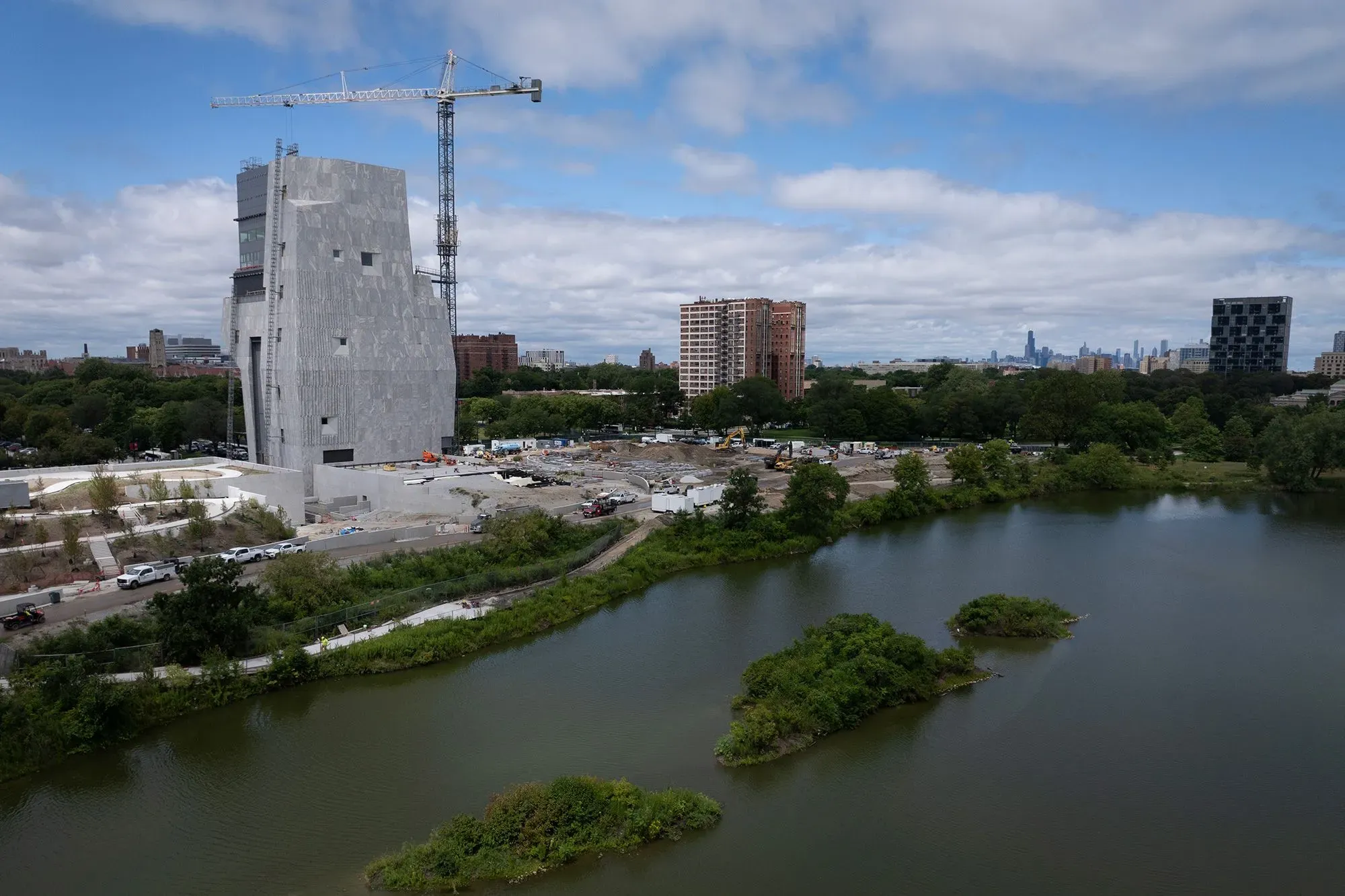 مركز أوباما الرئاسي قيد الإنشاء في شيكاغو، يظهر المبنى الحديث محاطًا بالطبيعة، مع مشهد للمدينة في الخلفية.