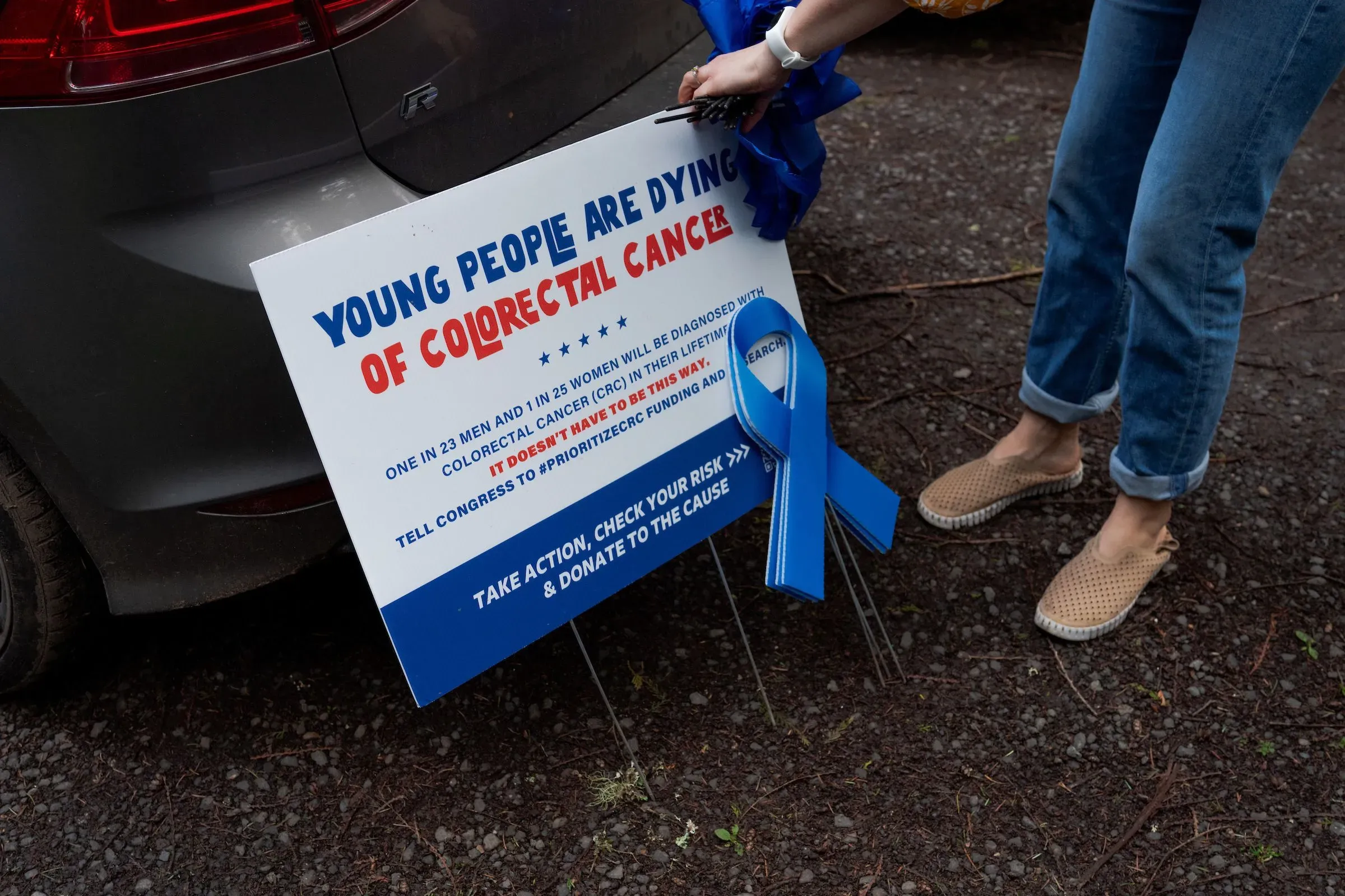 شخص يحمل لافتة تتحدث عن زيادة حالات سرطان القولون والمستقيم بين الشباب، مع إحصائيات تدعو للعمل من أجل الفحص والبحث.