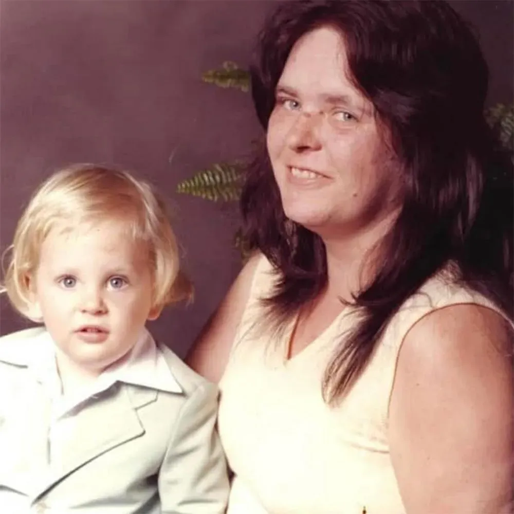 صورة تظهر امرأة تحمل طفلًا صغيرًا، حيث يبدو الطفل ذو شعر أشقر وعينين زرقاوين، بينما تبتسم المرأة. تعكس الصورة لحظة عائلية دافئة.