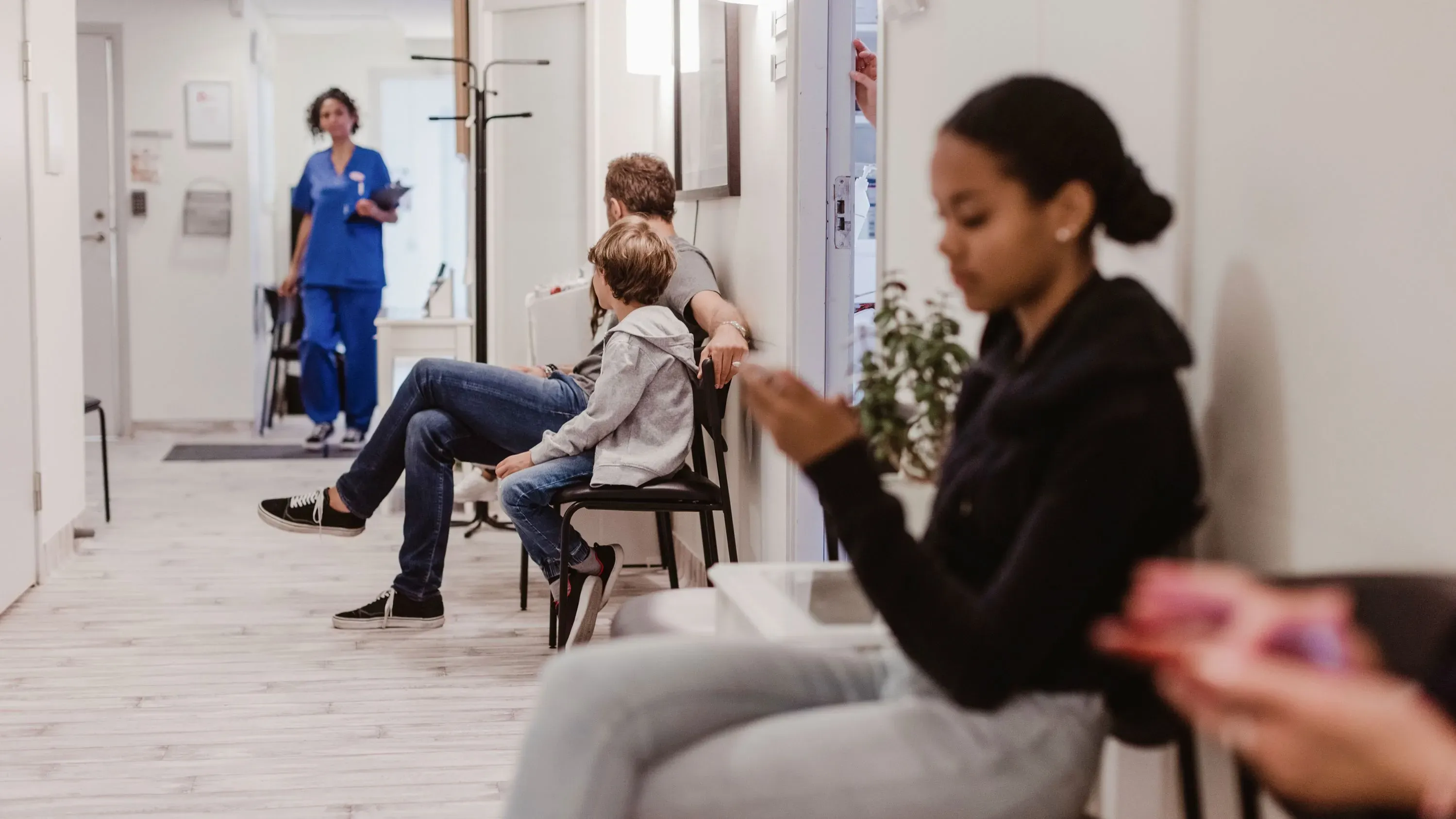 انتظارات المرضى في عيادة طبية، حيث يجلس مجموعة من الأفراد في قاعة الانتظار، بينما يخرج ممارس صحي.