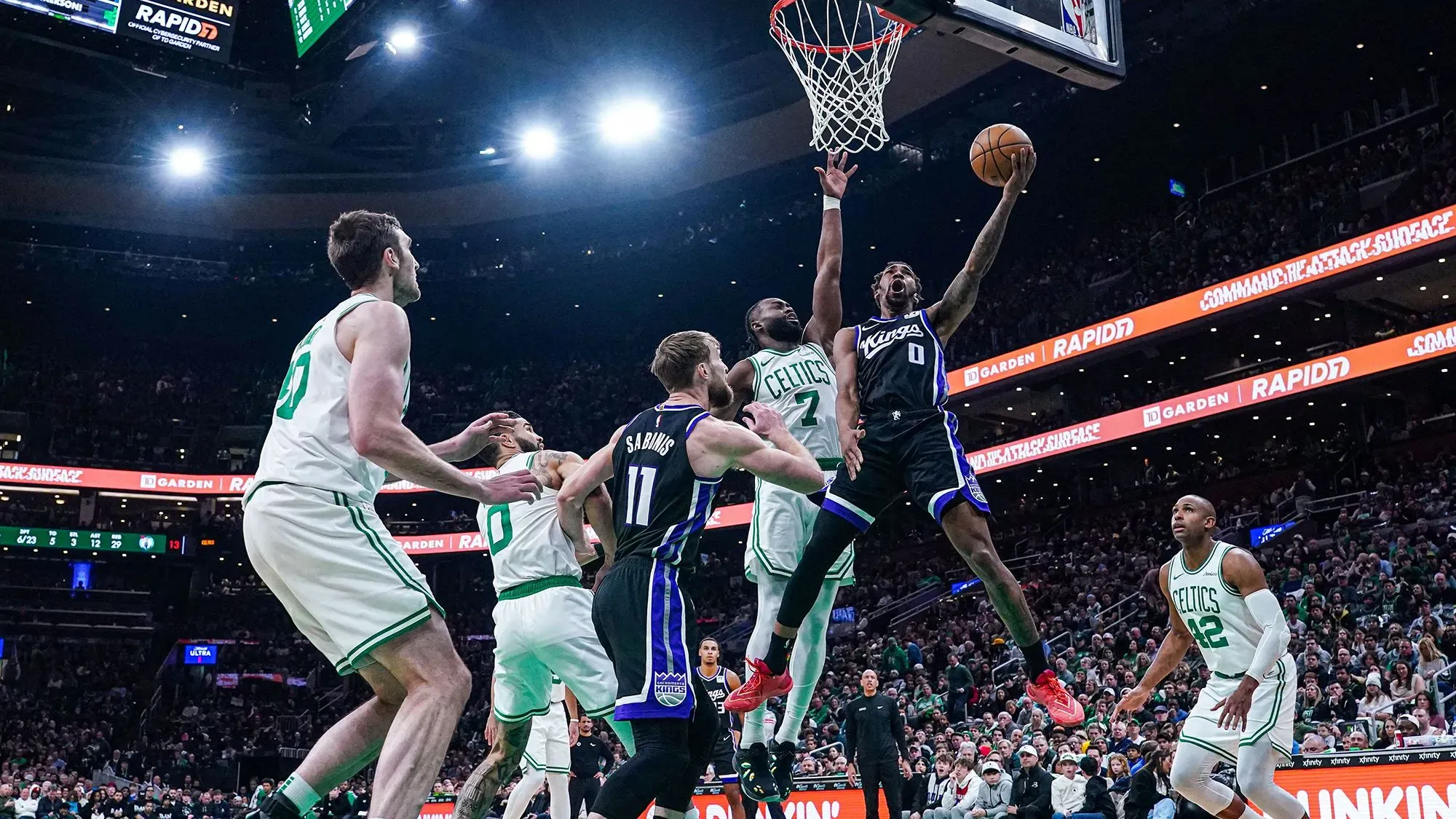 لاعب من فريق ساكرامنتو كينجز يسجل نقطة خلال مباراة مثيرة ضد بوسطن سلتكس، مع وجود لاعبين من الفريقين في الملعب.