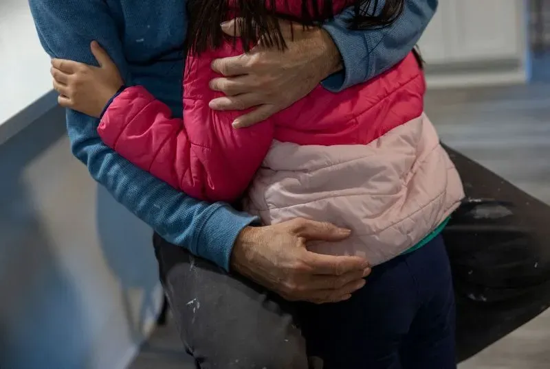 عناق دافئ بين والد وابنته الصغيرة، حيث ترتدي الفتاة سترة وردية، مما يعكس اللحظات الحميمية في عائلتهم في ظل التحديات.