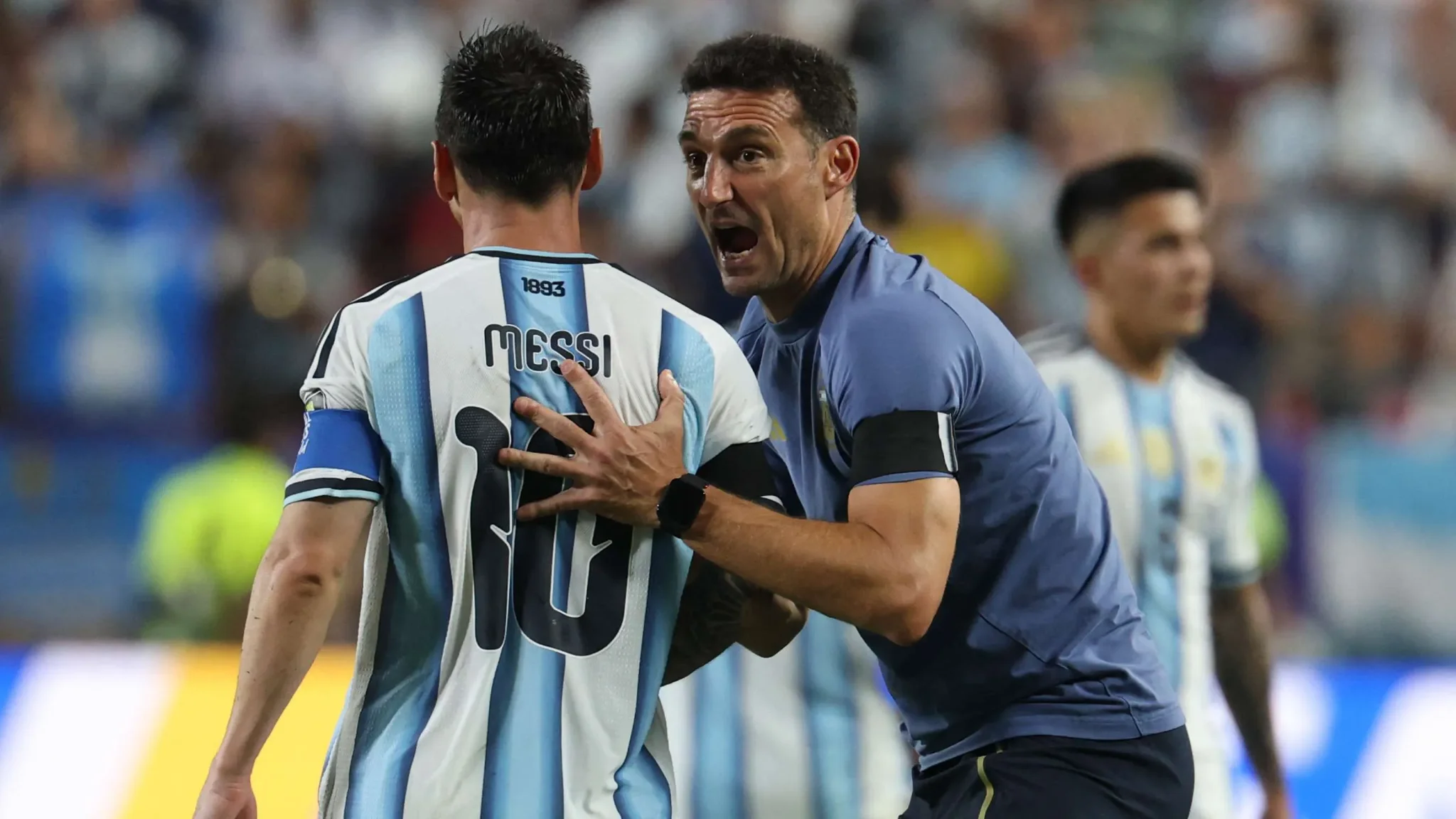 مدرب منتخب الأرجنتين يتحدث بحماس مع ليونيل ميسي خلال مباراة، في ظل تحديات إعادة بناء الفريق بعد رحيل ميسي.