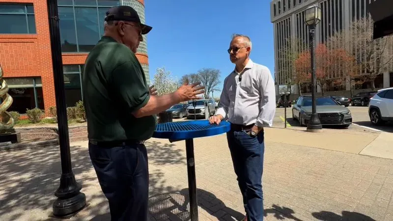 رجلان يتحدثان في شارع بمدينة ميشيغان، مع التركيز على تأثير التعريفات الجمركية على الاقتصاد المحلي.