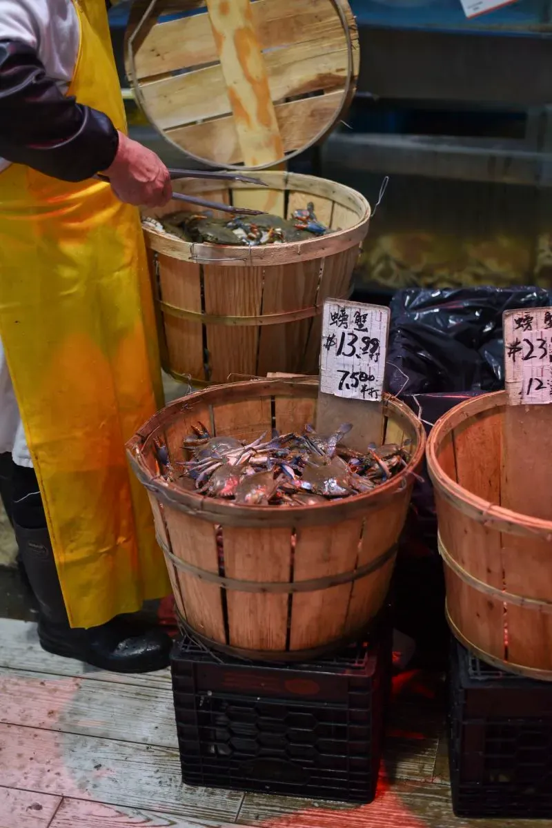 سلة خشبية تحتوي على سرطان البحر في سوبر ماركت تشانغ جيانغ، مع لافتات توضح الأسعار، تعكس تأثير الحرب التجارية على المنتجات المستوردة.