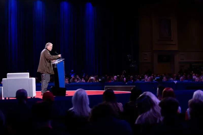 متحدث على المنصة خلال مؤتمر "CPAC"، مع جمهور كبير في الخلفية، وسط إضاءة زرقاء وأجواء سياسية محافظة.