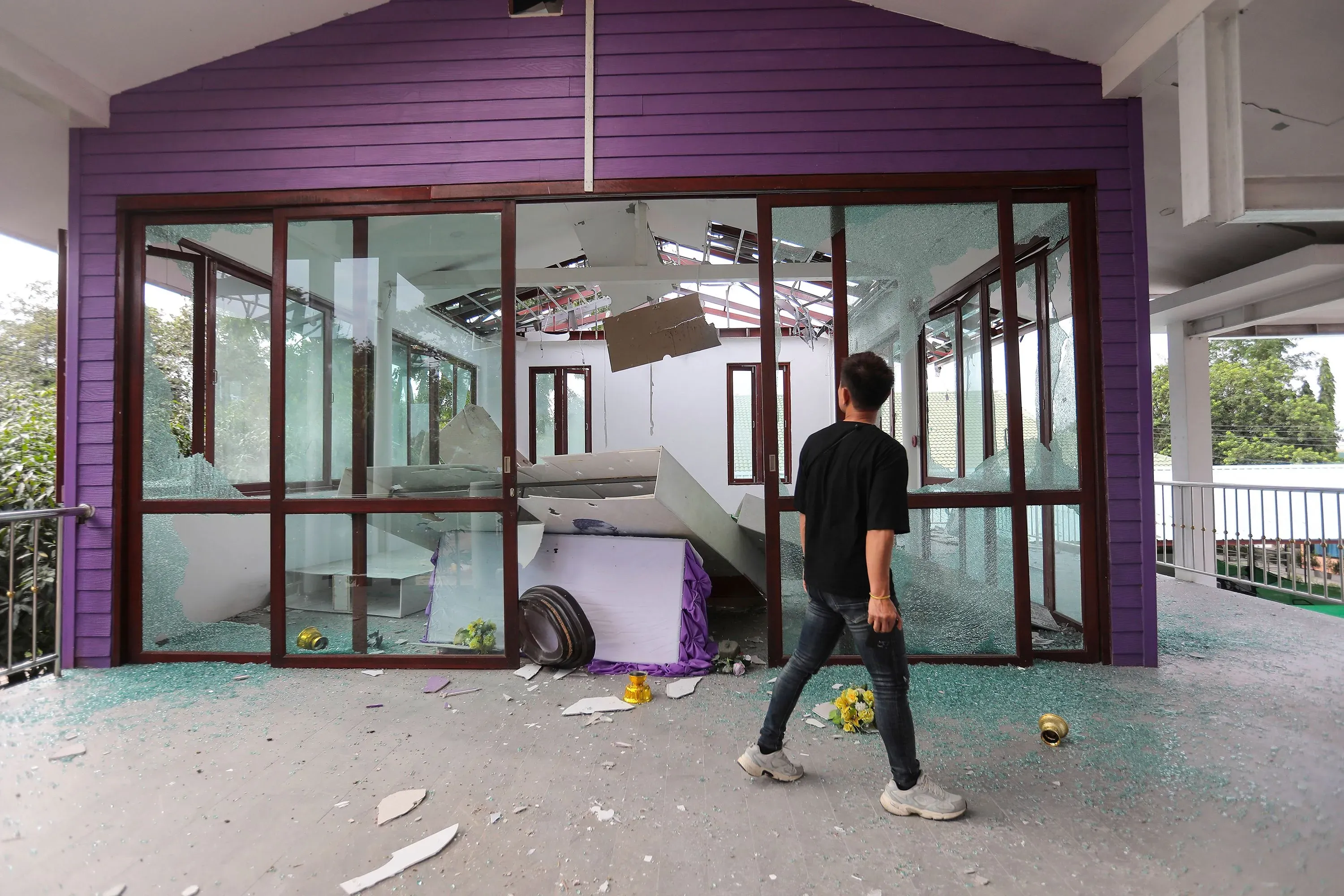 تظهر الصورة شخصًا يقف أمام منزل متضرر، حيث تحطم الزجاج والأثاث متناثر، مما يعكس آثار الاشتباكات المسلحة على الحدود بين تايلاند وكمبوديا.