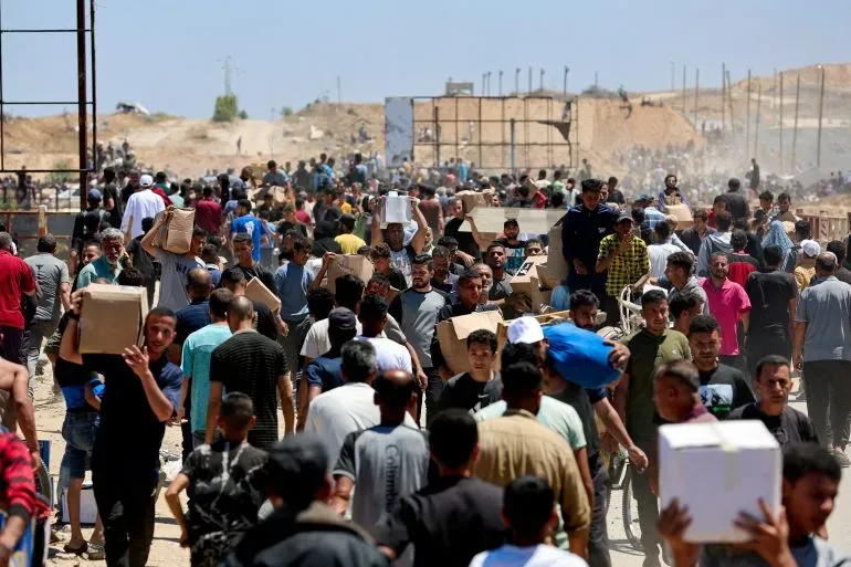 حشود كبيرة من الفلسطينيين في مركز توزيع المساعدات بغزة، يحملون صناديق الإغاثة وسط حالة من الفوضى والازدحام الشديد.