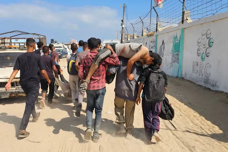 مجموعة من الشبان يحملون مصابًا في قطاع غزة، وسط مشهد مأساوي يعكس تأثير الهجمات الإسرائيلية على المدنيين أثناء محاولتهم الحصول على المساعدات.