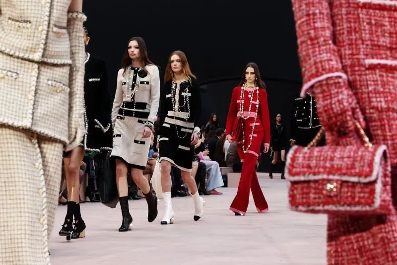 عرض أزياء في أسبوع الموضة في باريس، حيث تسير عارضات بأزياء أنيقة تتضمن تصاميم كلاسيكية مع لمسات عصرية، مع التركيز على الأقمشة الفاخرة.