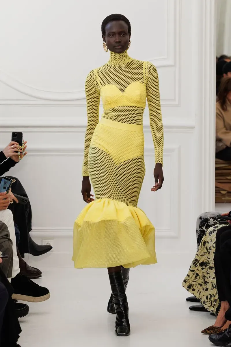 عارضة أزياء ترتدي فستاناً أصفر شبكي مع تنورة منفوشة، تسير على المنصة خلال عرض أزياء في أسبوع الموضة في باريس.