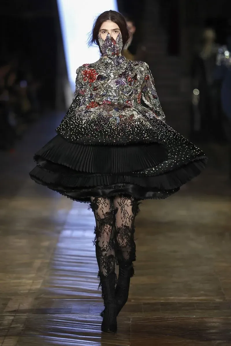 عرض أزياء يظهر عارضة ترتدي فستاناً مزخرفاً بألوان زاهية مع تنورة واسعة، تعكس تأثيرات الموضة المعاصرة.