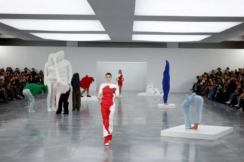 عرض أزياء مبتكر خلال أسبوع الموضة في باريس، حيث تسير عارضات يرتدين تصاميم ملونة وجرئية، مع جمهور يشاهد في الخلفية.