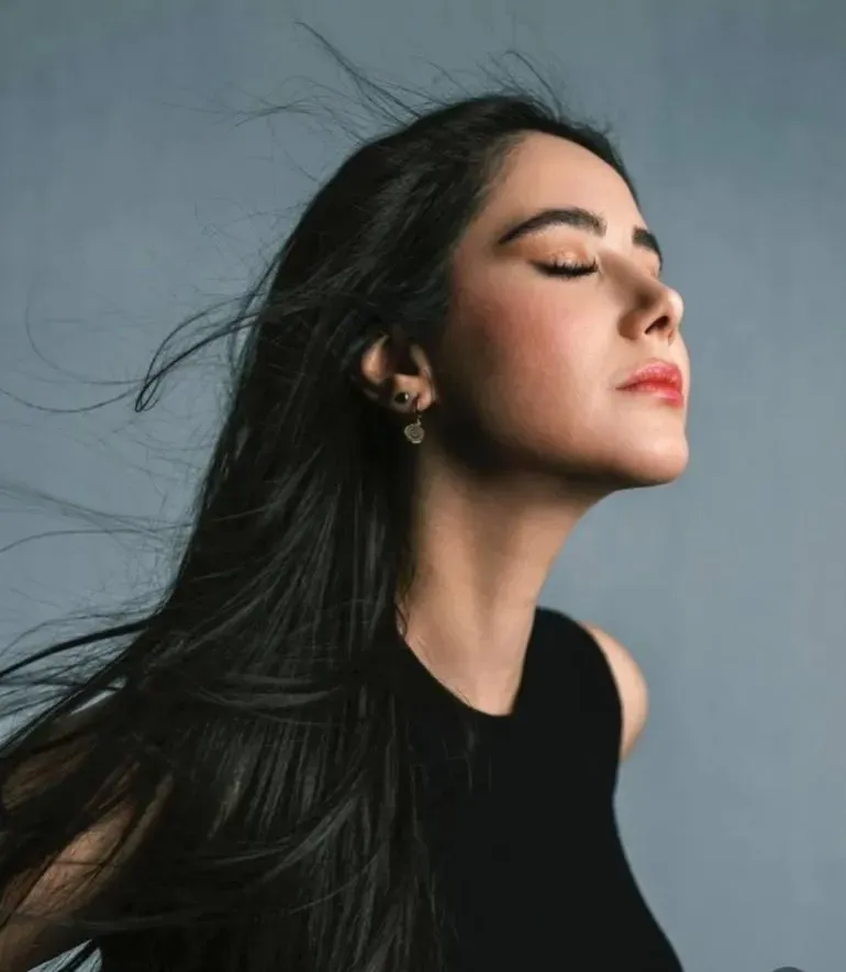 امرأة شابة ذات شعر أسود طويل، تغلق عينيها وتتنفس بعمق، تعبر عن لحظة من الهدوء في ظل الأوضاع المتوترة في طهران.