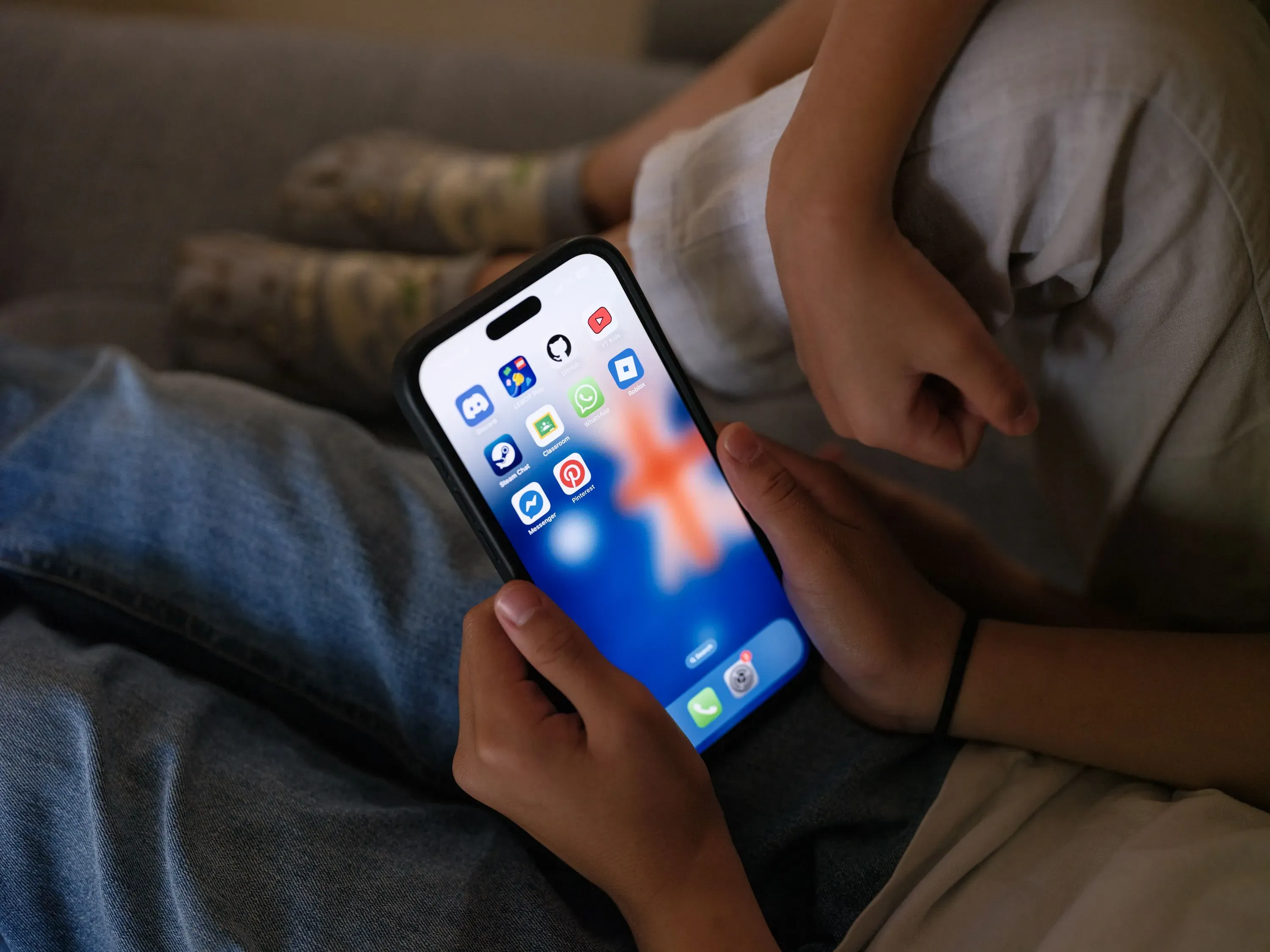 هاتف ذكي يحمل تطبيقات وسائل التواصل الاجتماعي، مع يد طفل تحتضنه، يعكس تأثير الحظر الأسترالي على الأطفال دون سن 16 عامًا.