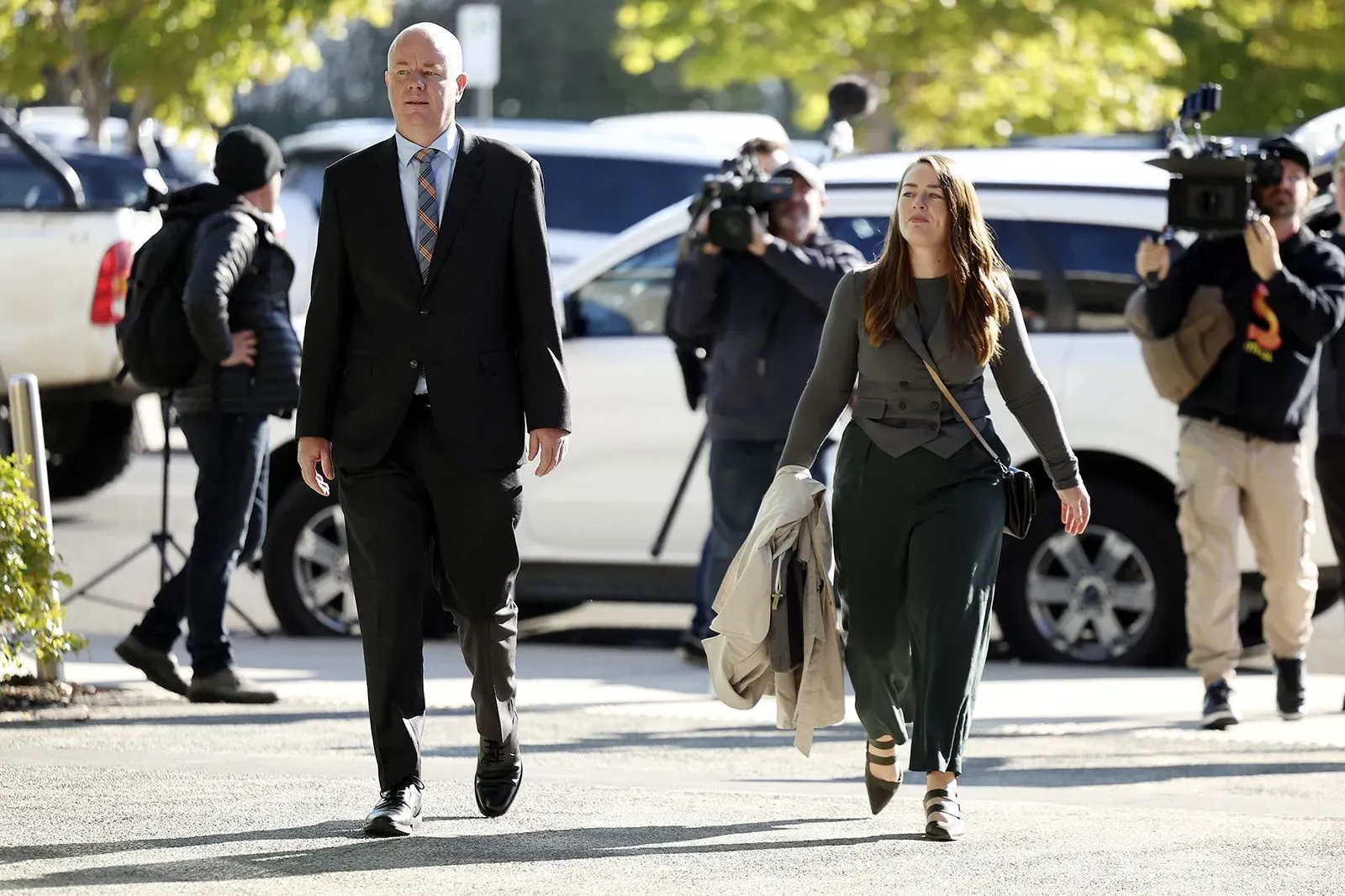 امرأة ترتدي ملابس رسمية تسير مع رجل في بدلة، محاطان بمصورين، خارج محكمة في أستراليا، وسط قضية قتل مثيرة للجدل.