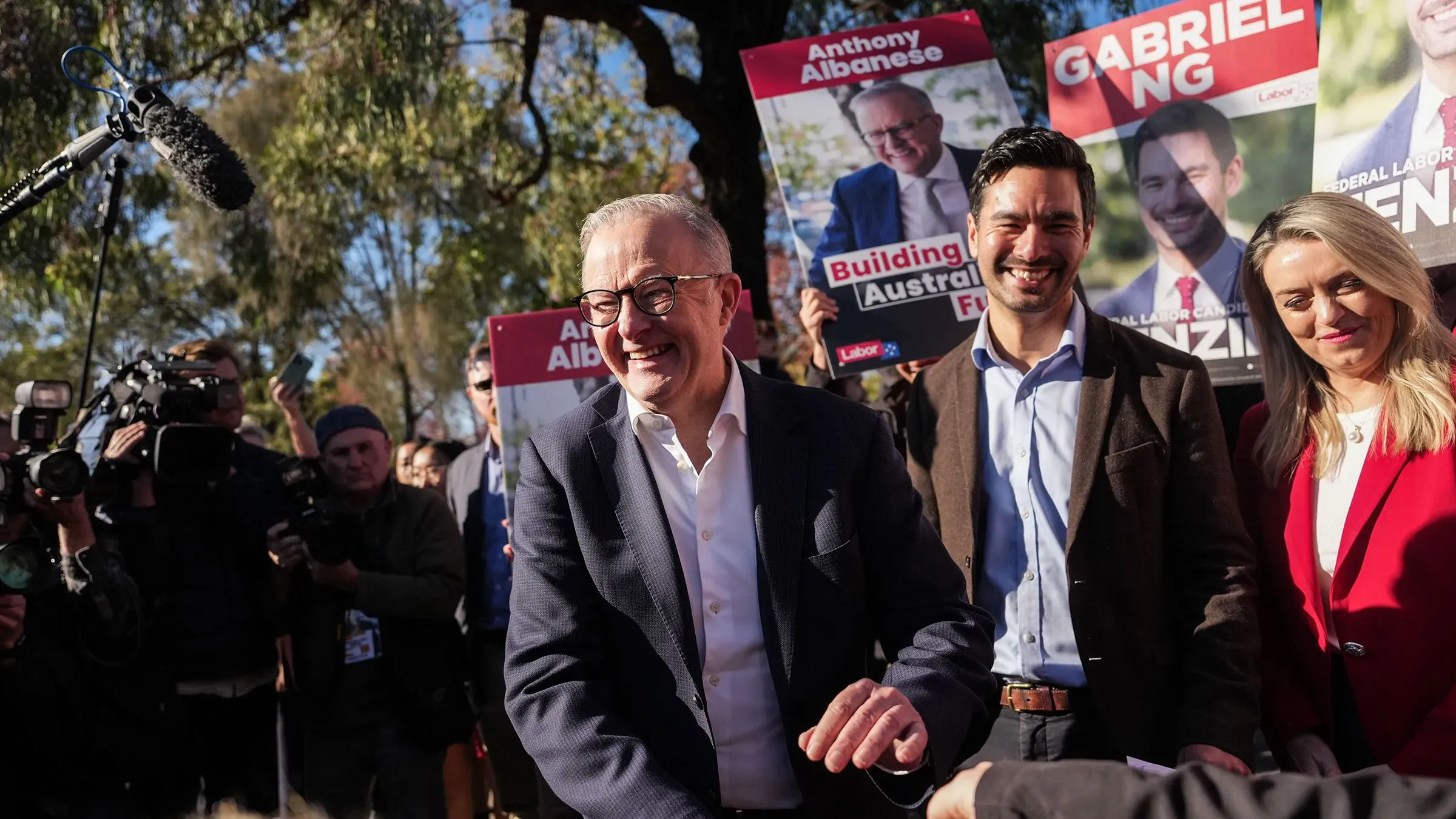 رئيس الوزراء الأسترالي أنتوني ألبانيز مبتسم وسط مؤيديه، مع لافتات دعائية لحزبه، مما يعكس أجواء الحملة الانتخابية.