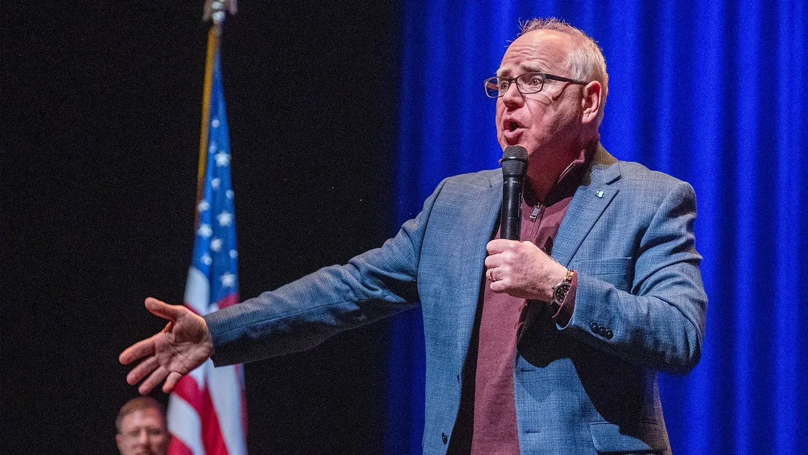 حاكم مينيسوتا تيم والز يتحدث في مسرح بأو كلير، ويسكونسن، مع العلم الأمريكي خلفه، معبرًا عن قلقه بشأن السياسة الحالية.