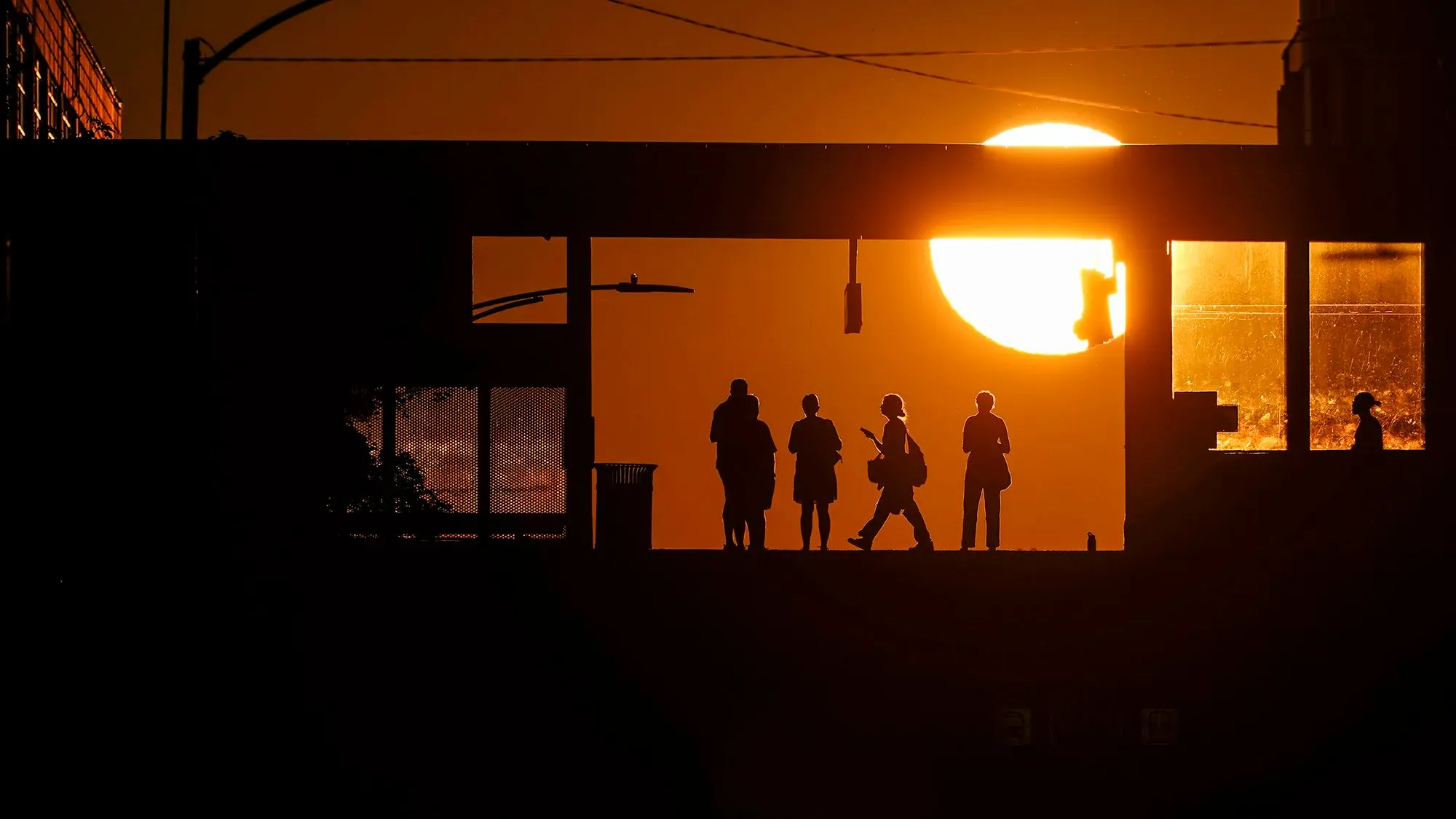 ظل silhouettes لأشخاص يقفون في محطة، مع شمس غاربة خلفهم، مما يرمز إلى التحديات التي يواجهها الشباب في سوق العمل.